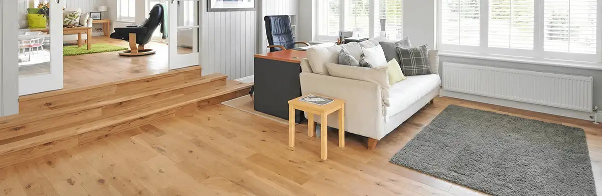 A modern living room with professionally installed laminate flooring, a beige sofa, a small side table, a gray rug, and large windows with white shutters in Tempe, AZ